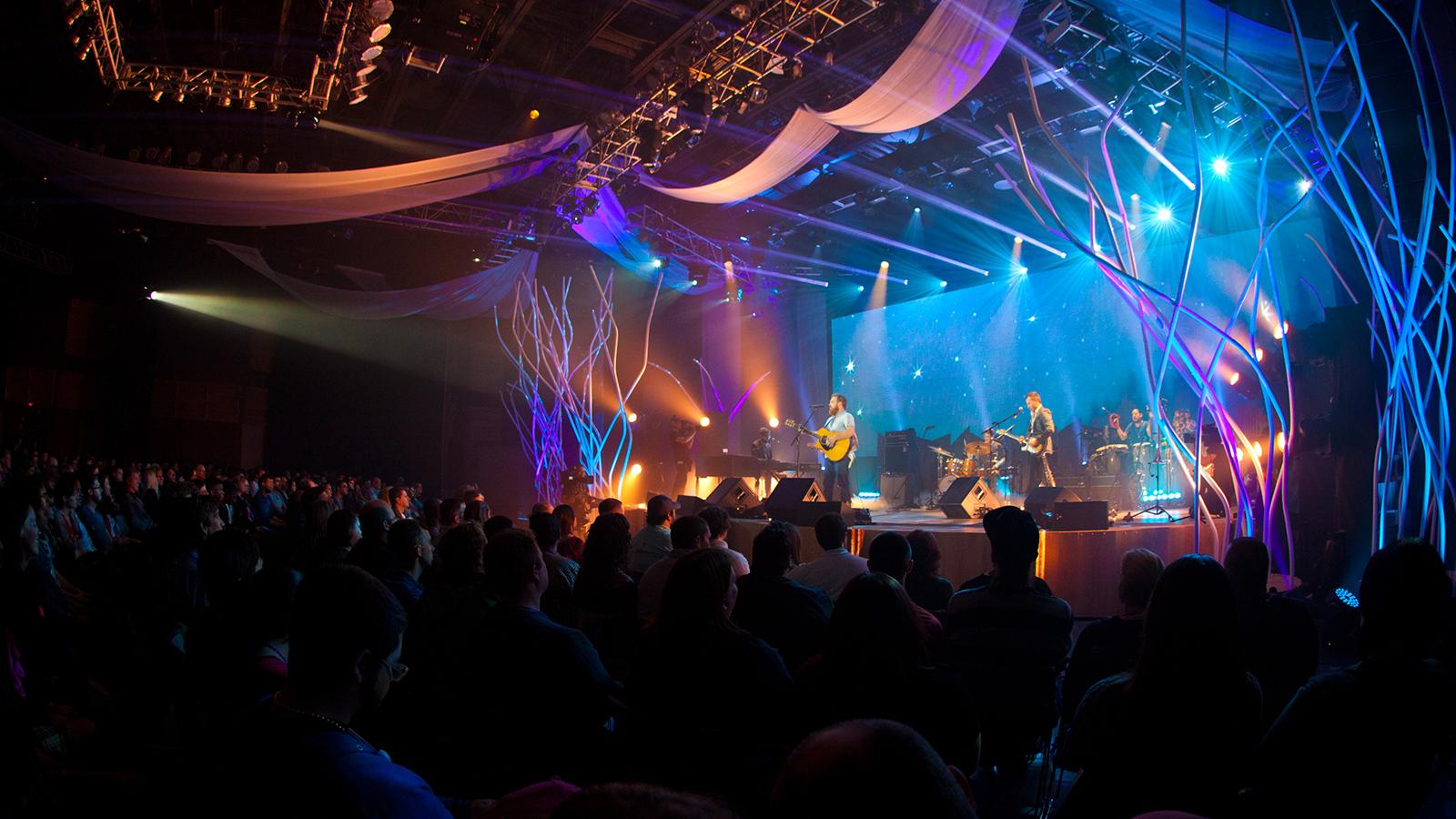 乐队在一个大音乐厅演奏音乐, 黑暗的礼堂里有几盏明亮的蓝色和紫色的灯指向舞台.
